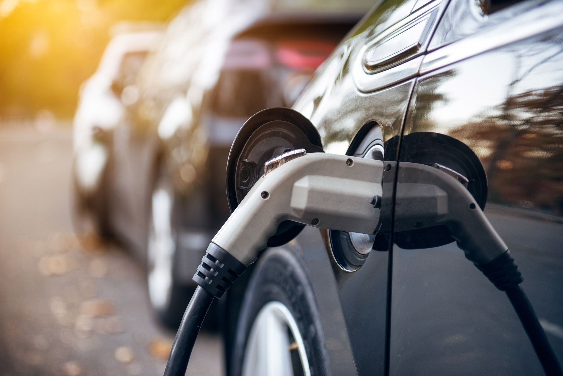 Electric car charging on parking lot with electric car charging station on city street. Electric cars in the row ready for charge. Close up of the power supply plugged into an electric car being charged.&#xD;