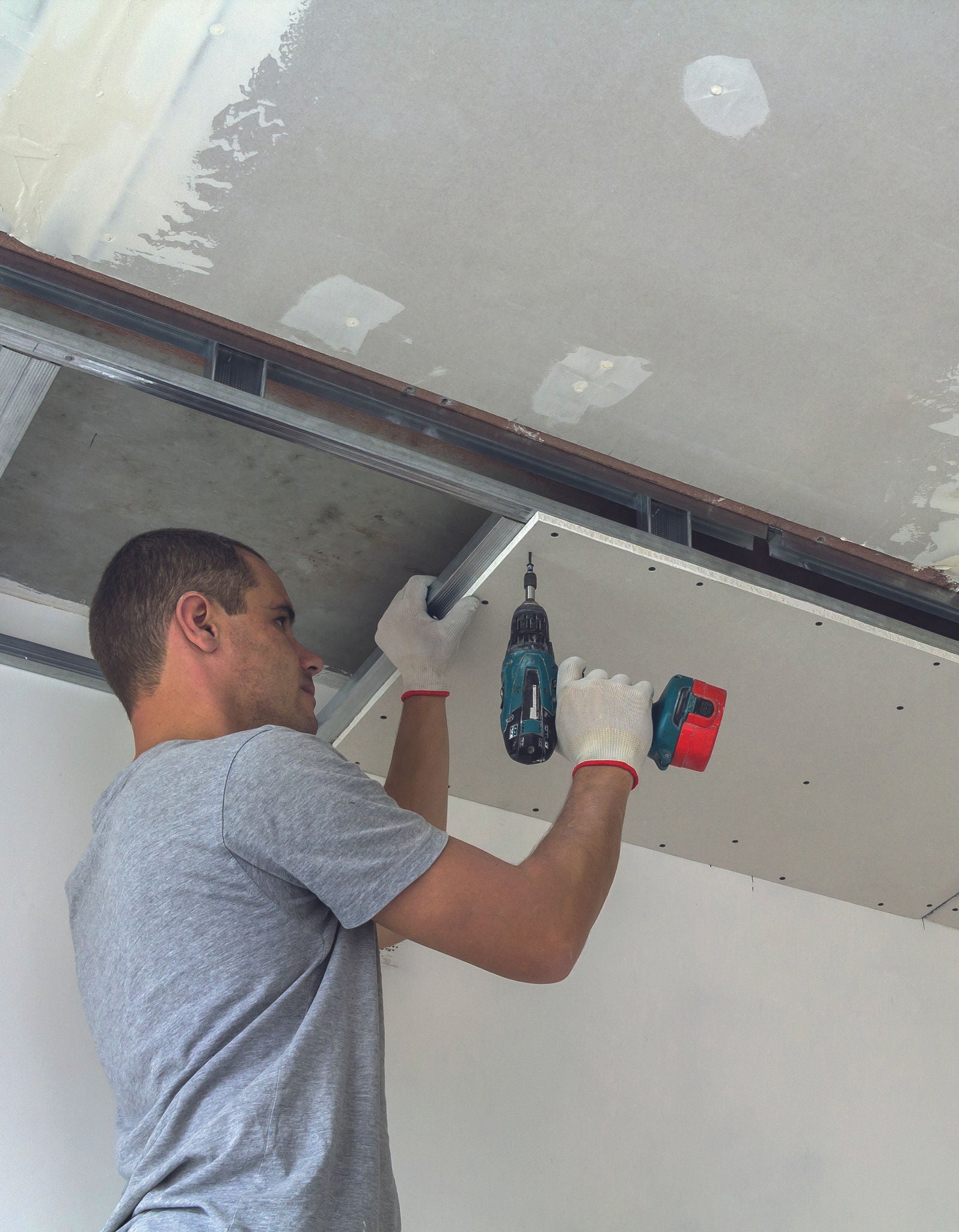 Construction worker assemble a suspended ceiling with drywall and fixing the drywall to the ceiling metal frame with screwdriver.