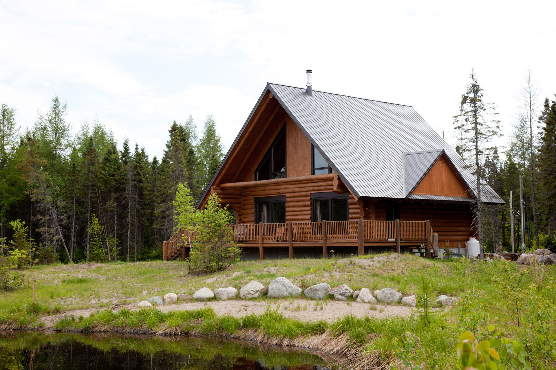 Large wood and stone log home surrounded by a cloudy sky and a lake.