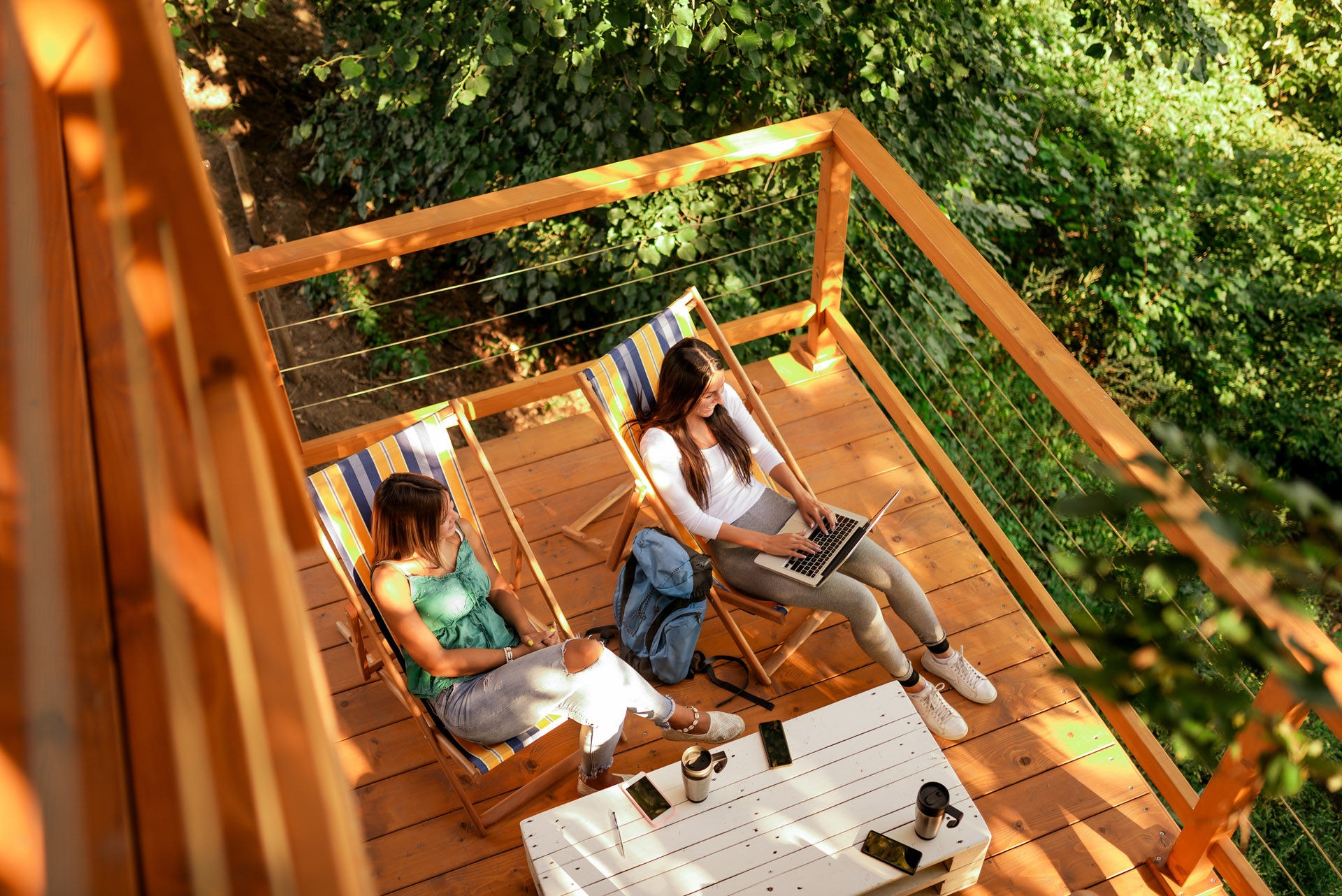 High angle image of two young women enjoying on a wooden cabin terrace in forest.